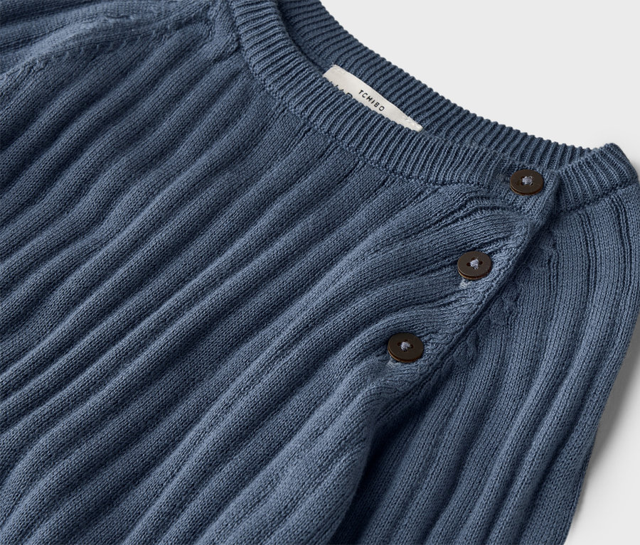 Egy sötétkék, bordázott kötött pulóver közeli képe, három gombbal a gallérján.