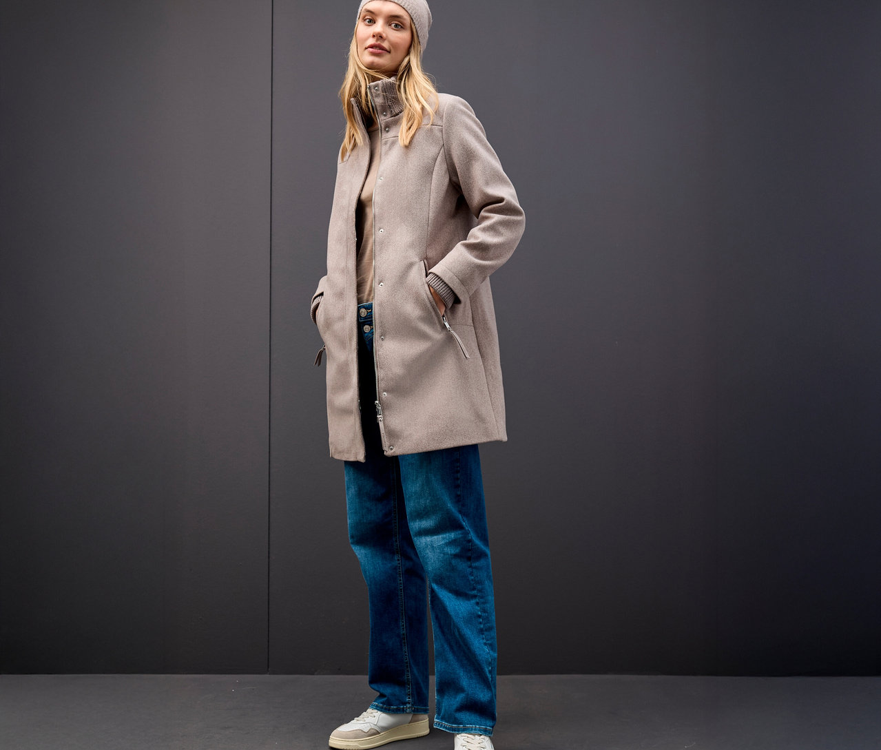 Nő bézs sapkában és Street One rövid kabátban, szürke háttér előtt.