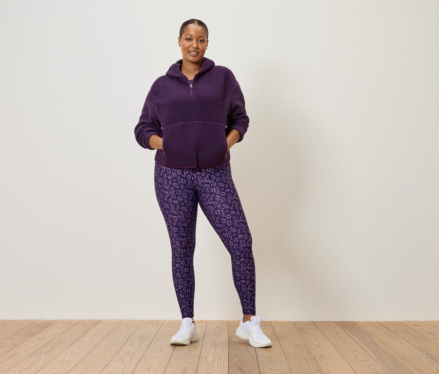 Nő lila, félcipzáras fleece pulóverben és lila leopárdmintás leggingsben, fehér tornacipőben.