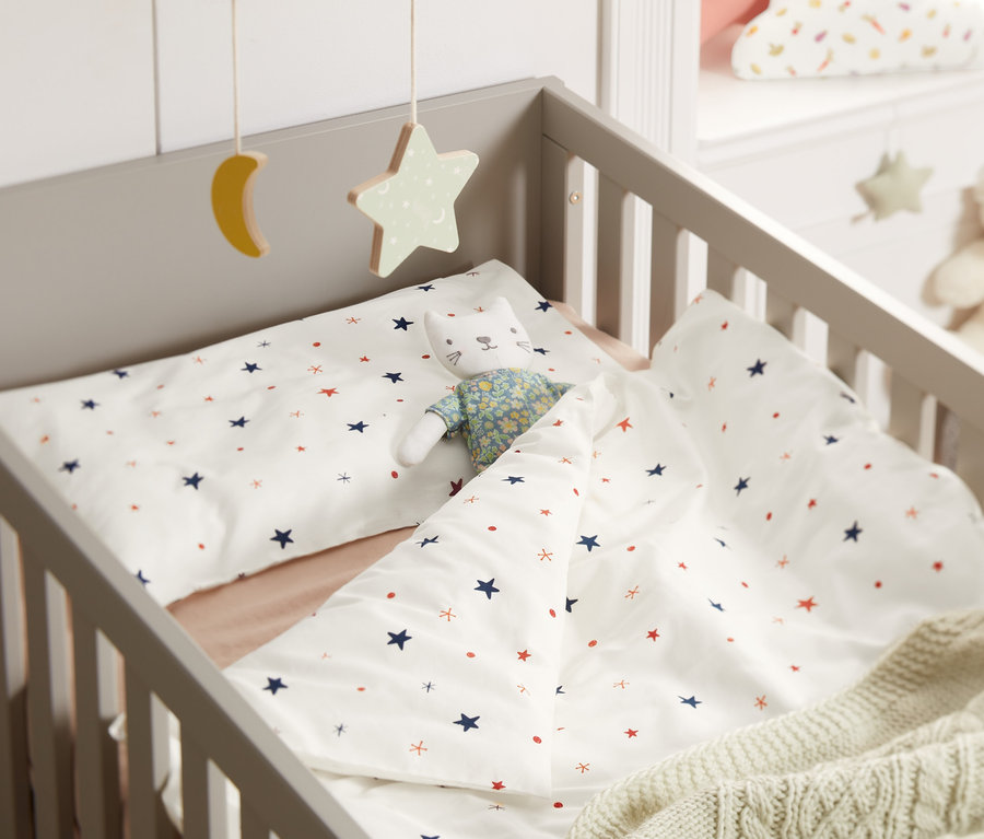 A kiságyban csillagos gyerek renforcé ágynemű és egy macska játék.