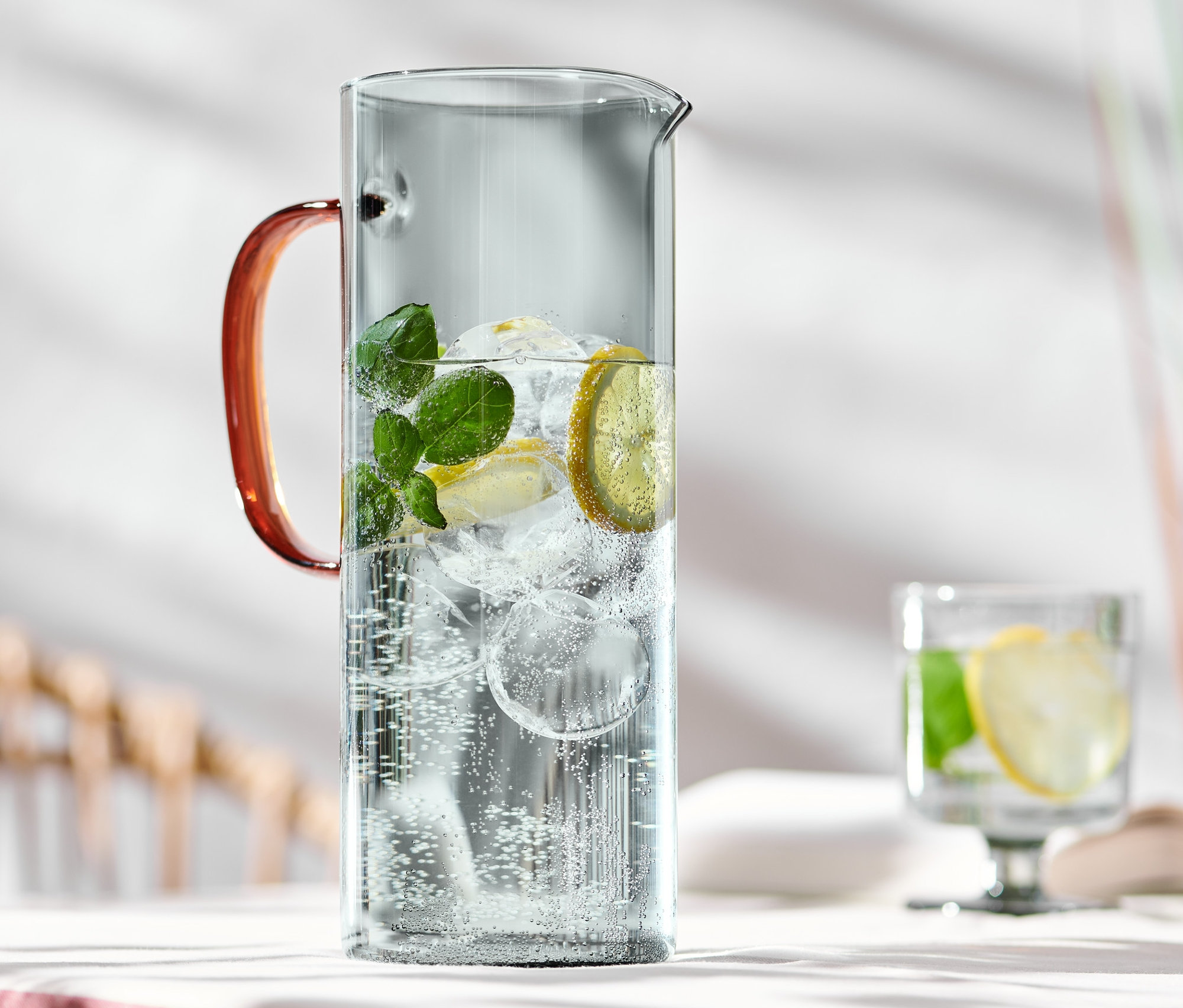 Egy üvegkancsó víz, jég, citrom és menta az asztalon.