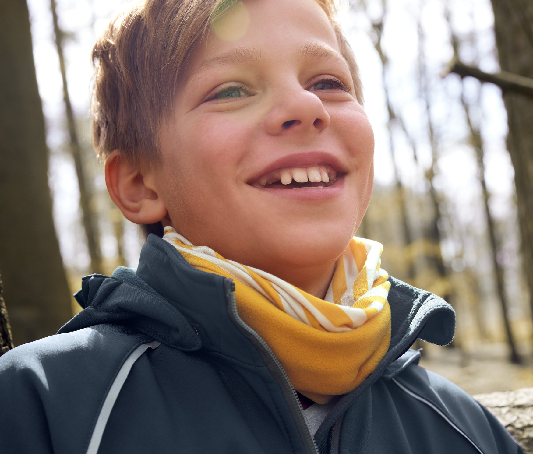 Mosolygó fiú softshell dzsekit és multifunkcionális kendőt visel.