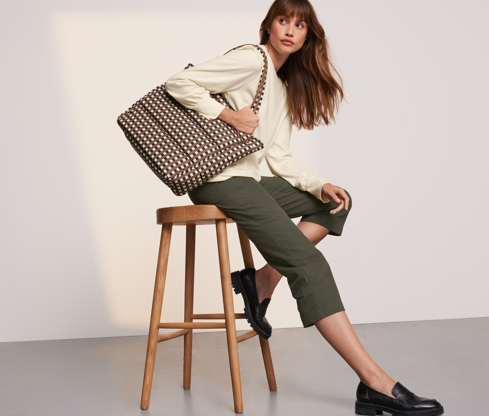 Nő ül egy széken, a vállán egy steppelt táska.