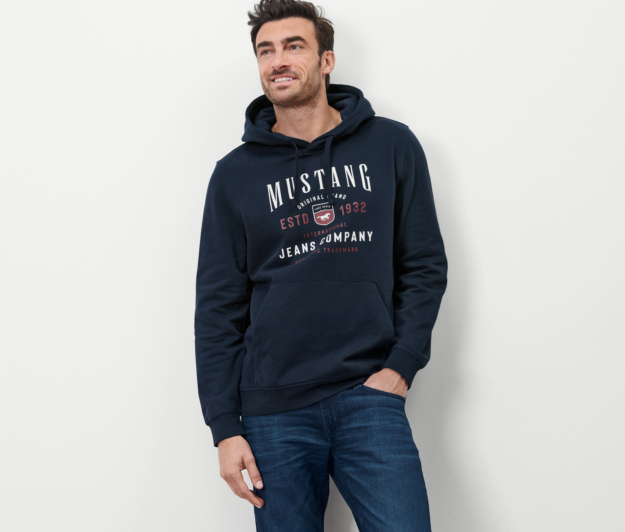 Férfi pózol sötétkék »Mustang« kapucnis felsőben és farmerban.
