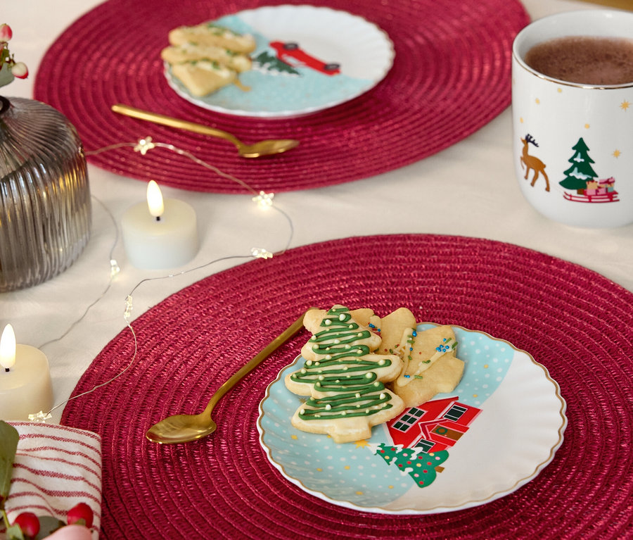 Két asztal piros tányéralátétekkel, rajtuk arany dekorációjú desszertes tányérok, süteménykiszúrók és arany kanalak.