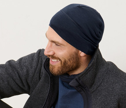 Férfi ül a fapadlón, és sötétkék, merinógyapjú unisex sapkát visel.