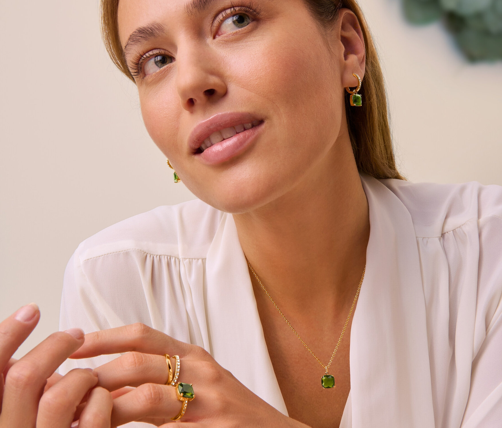 Nő visel Forest nyakláncot zöld üvegkristállyal, Forest karika fülbevalót zöld üvegkristállyal, Forest gyűrűt zöld üvegkristállyal és Double Wave gyűrűt üvegkristályokkal.