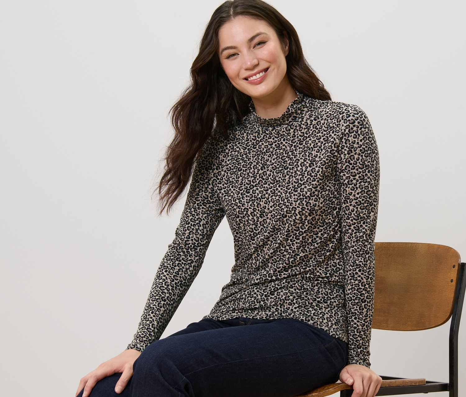 Nő ül egy széken, állógalléros, nyomott mintás pólóblúzt visel.