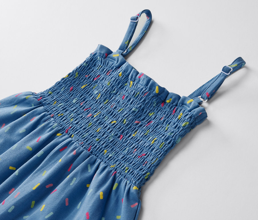 Kék, 7/8-os kezeslábas közelről, színes mintákkal, fehér háttéren.