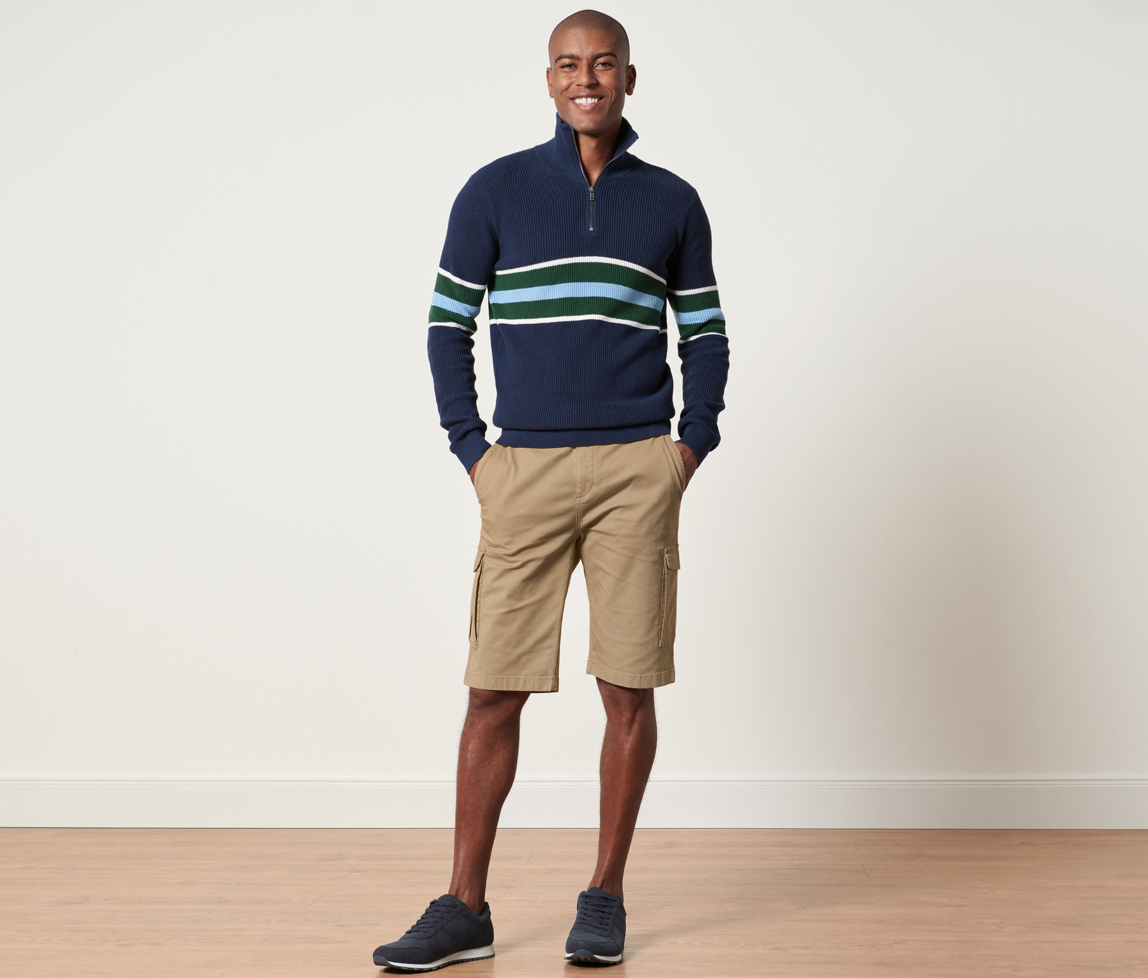 Férfi áll és pózol tengerészkék csíkos pulóverben és homokszínű oldalzsebes rövidnadrágban.