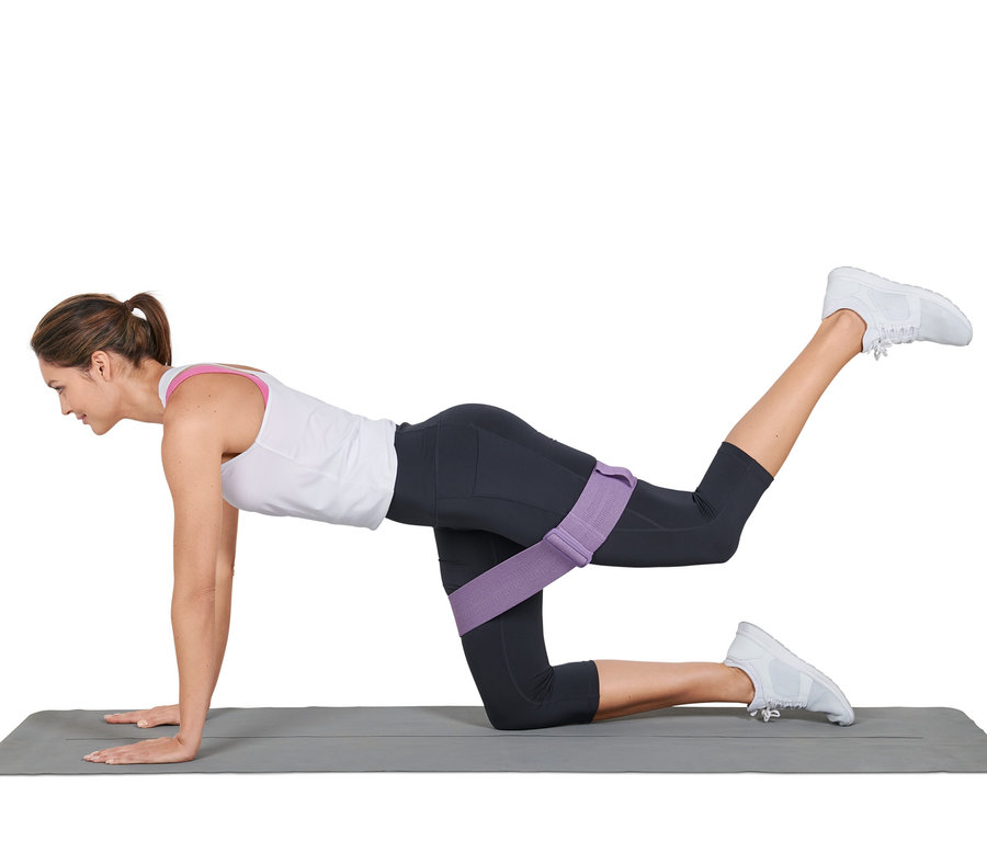 Nő gyakorlatokat végez egy szőnyegen egy rugalmas, állítható fitneszszalaggal.