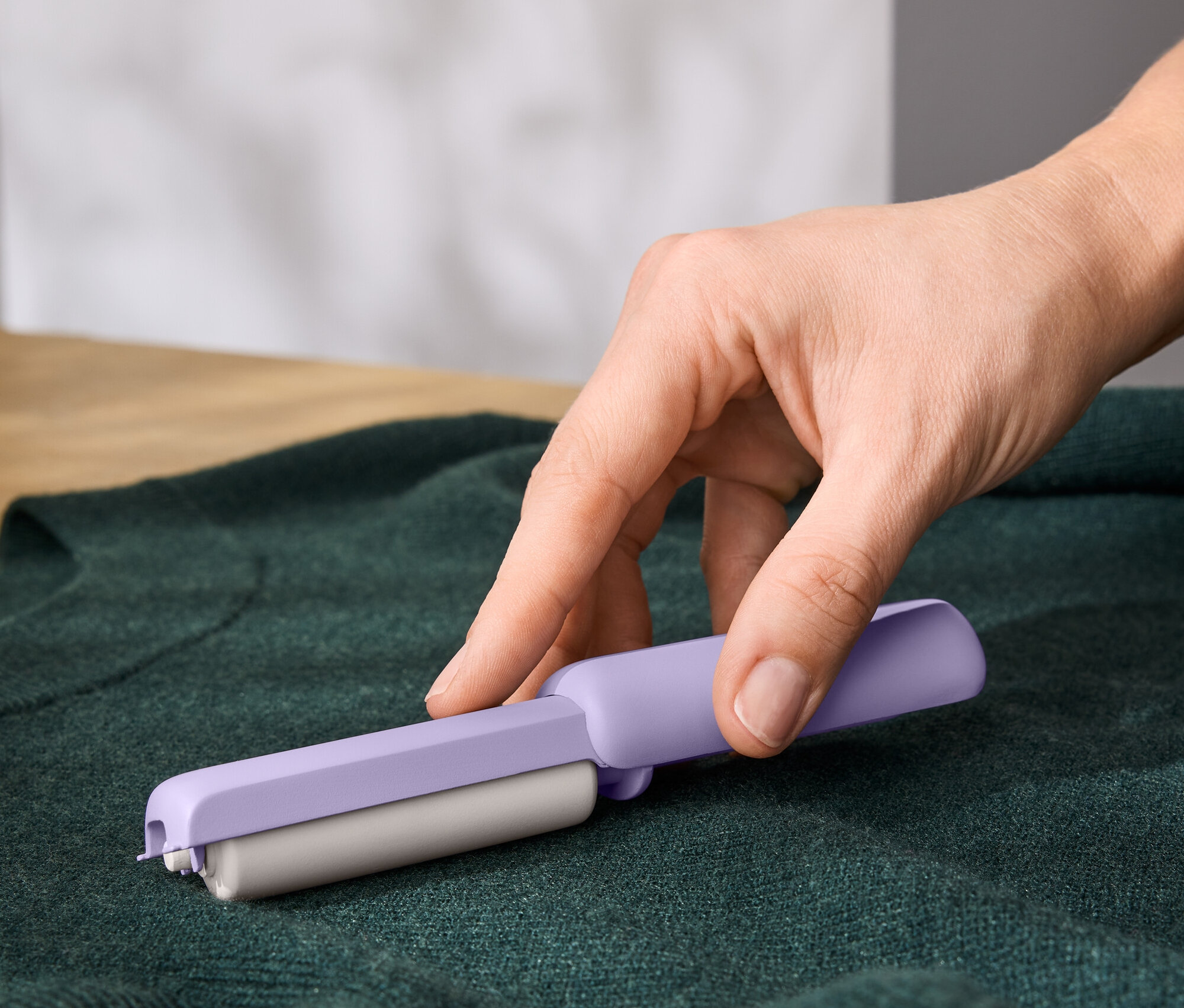 Egy kéz egy lila szöszeltávolítót használ egy zöld pulóveren.