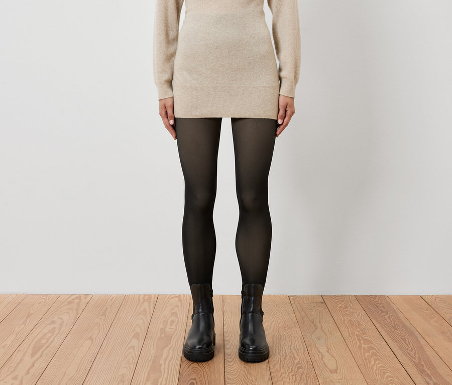 A nő bézs ruhát, fekete harisnyát és fekete csizmát visel.