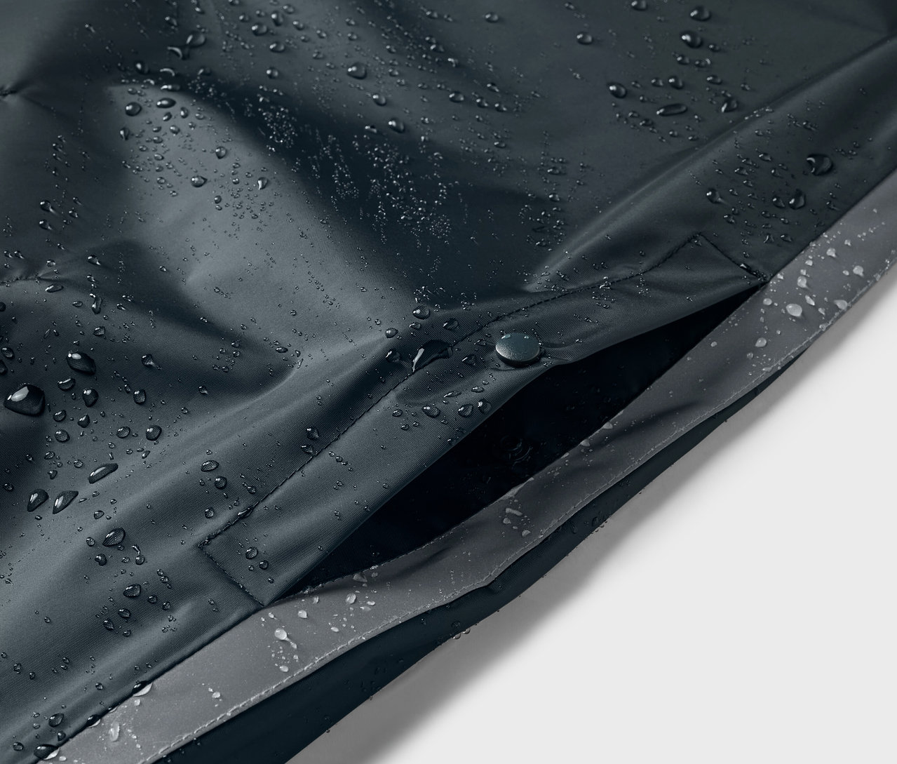 Kék gyerek esőponcsó részlete vízcseppekkel és zsebbel.