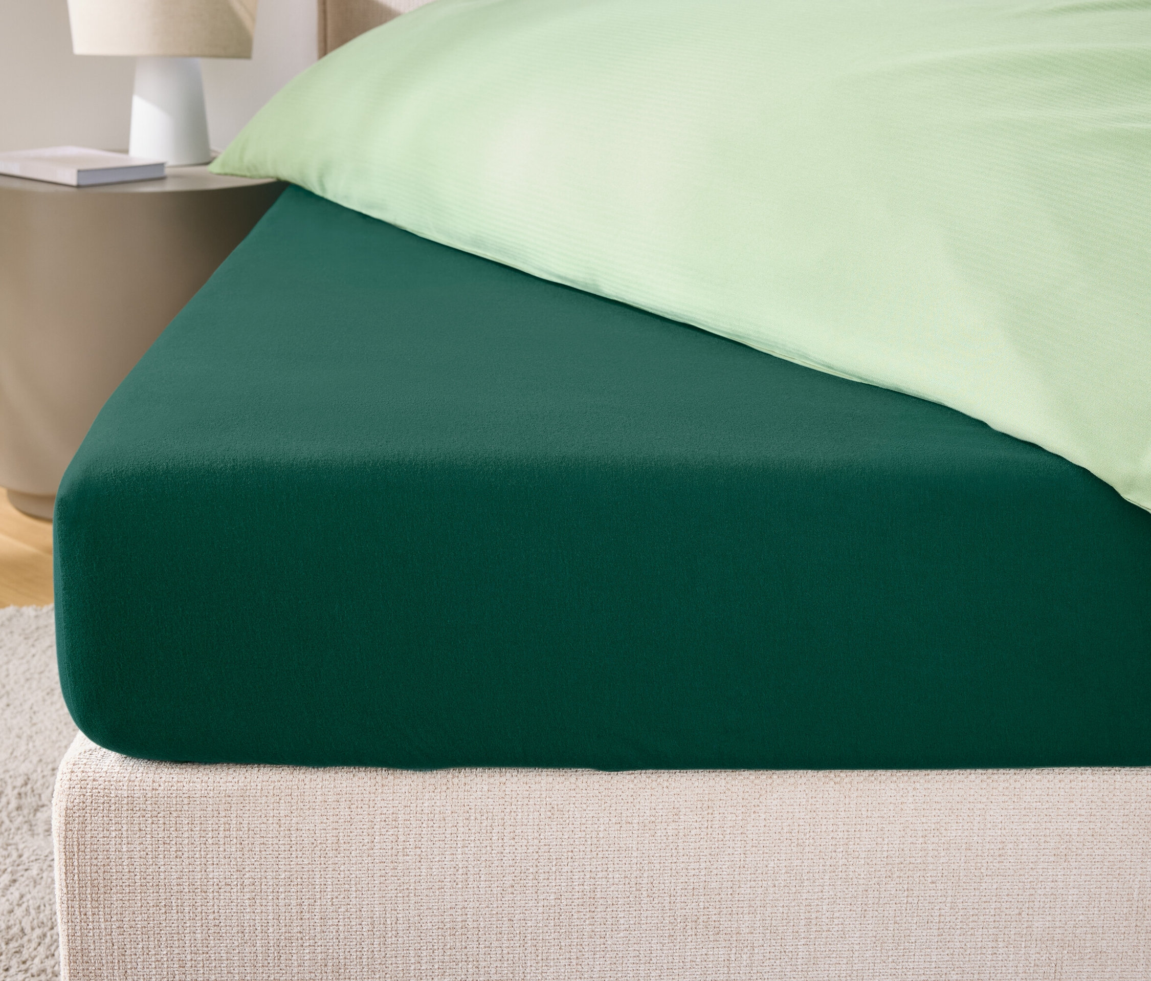 Egy zöld gumis lepedő közeli képe egy ágyon, krémszínű fejtámlával és világoszöld párnahuzattal.