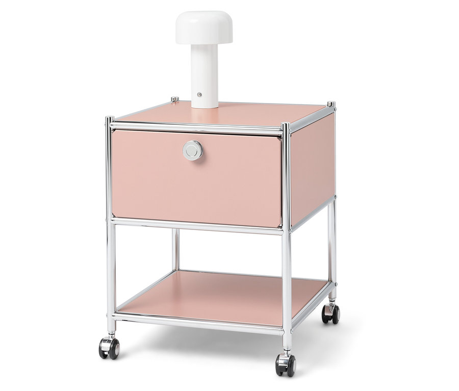 Rózsaszín éjjeliszekrény króm vázzal és fehér lámpával a tetején.