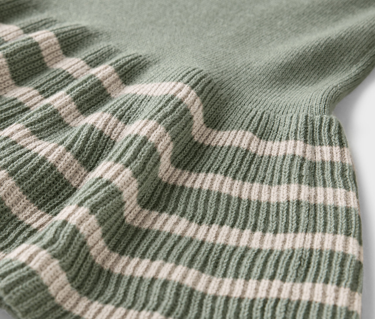Egy zöld pulóver részlete krémszínű csíkokkal.