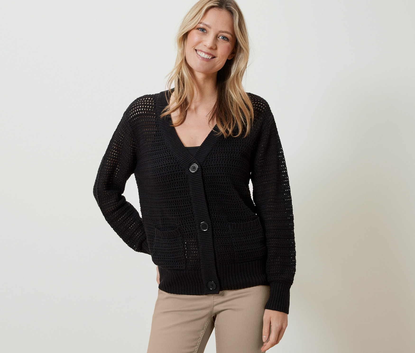 Nő visel fekete csipkekötésű kardigánt és bézs nadrágot.