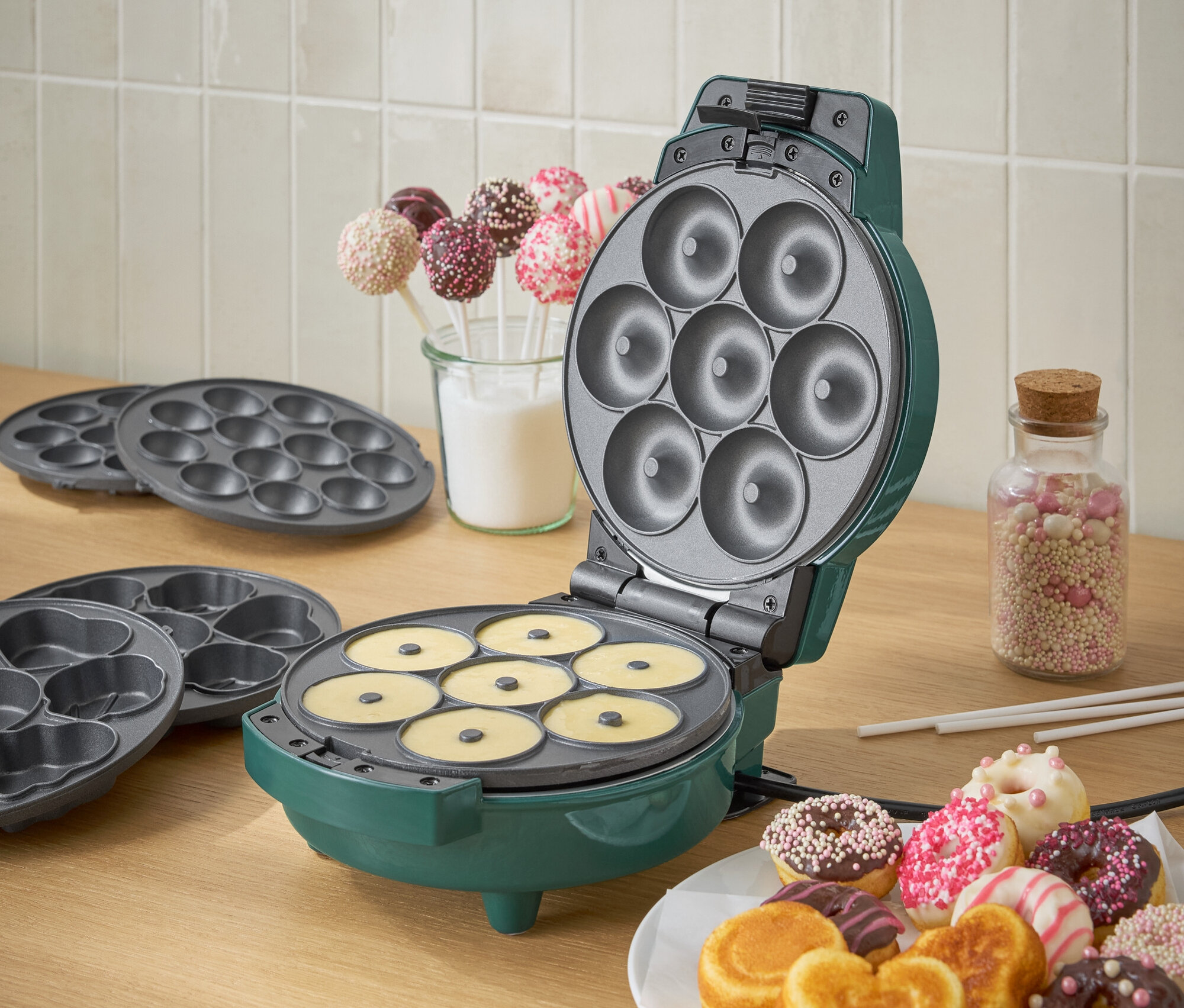 Zöld donutkészítő tésztával és egy tányér kész donuttal.