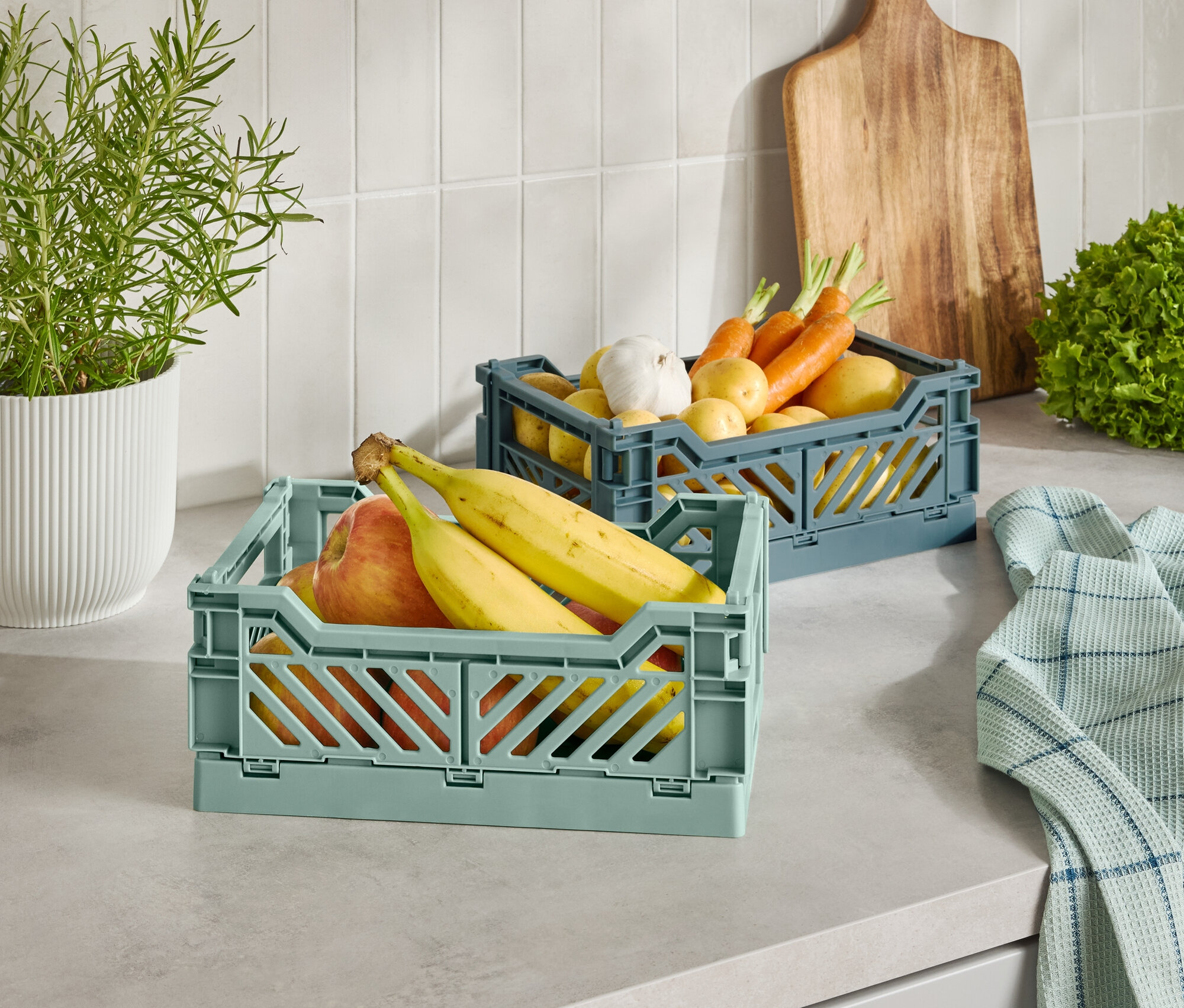 Két műanyag kosár gyümölccsel és zöldséggel egy konyhapulton.