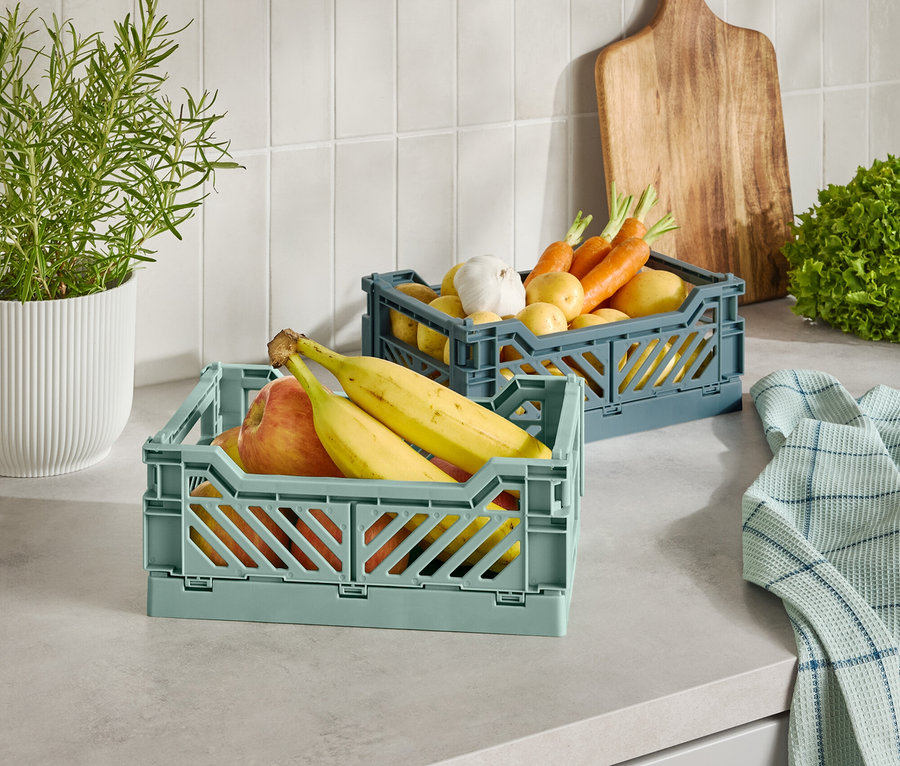 Két műanyag kosár gyümölccsel és zöldséggel egy konyhapulton.