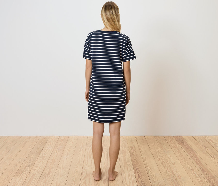 Egy nő áll háttal a kamerának, kék-fehér csíkos pólóruhát visel.