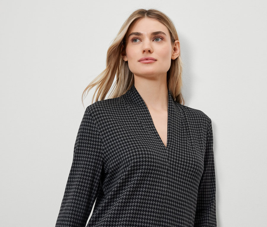 Egy szőke nő fekete-szürke, houndstooth mintás, V-nyakú ruhát visel.