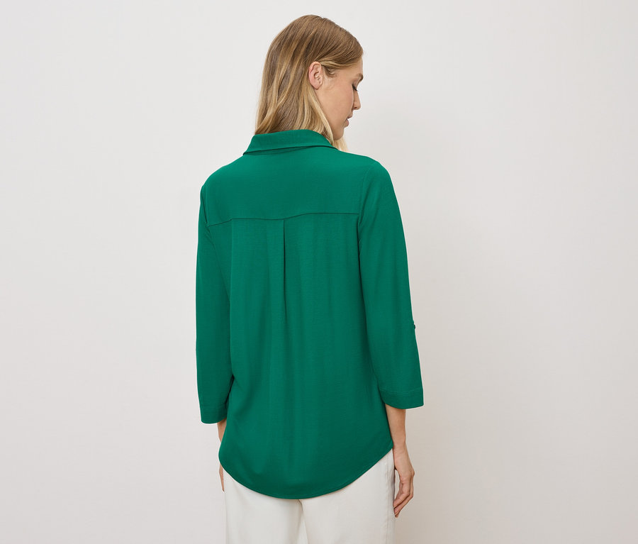 A nő háttal a kamerának zöld inget és fehér nadrágot visel.