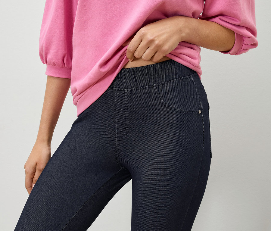 Nő rózsaszín pulóvert tart sötétkék farmer leggings felett.