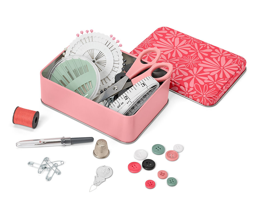 Nyitott fém doboz varrókészlettel, mellette egy orsó cérna, egy gyűszű, gombostűk, gombok és egy tűbefűző.