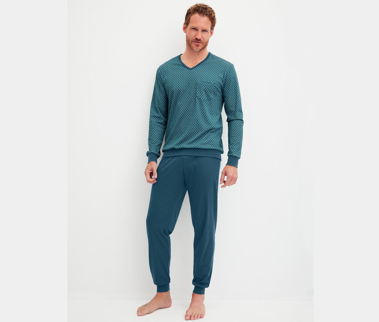 Egy férfi áll mezítláb egy fehér fal előtt, sötétkék pizsamában.