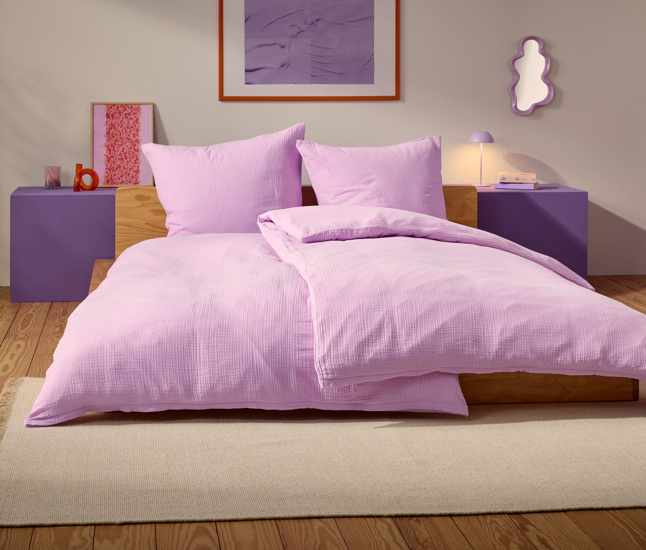 Egy lila ágy két párnával és egy takaróval egy bézs szőnyegen áll egy hálószobában.