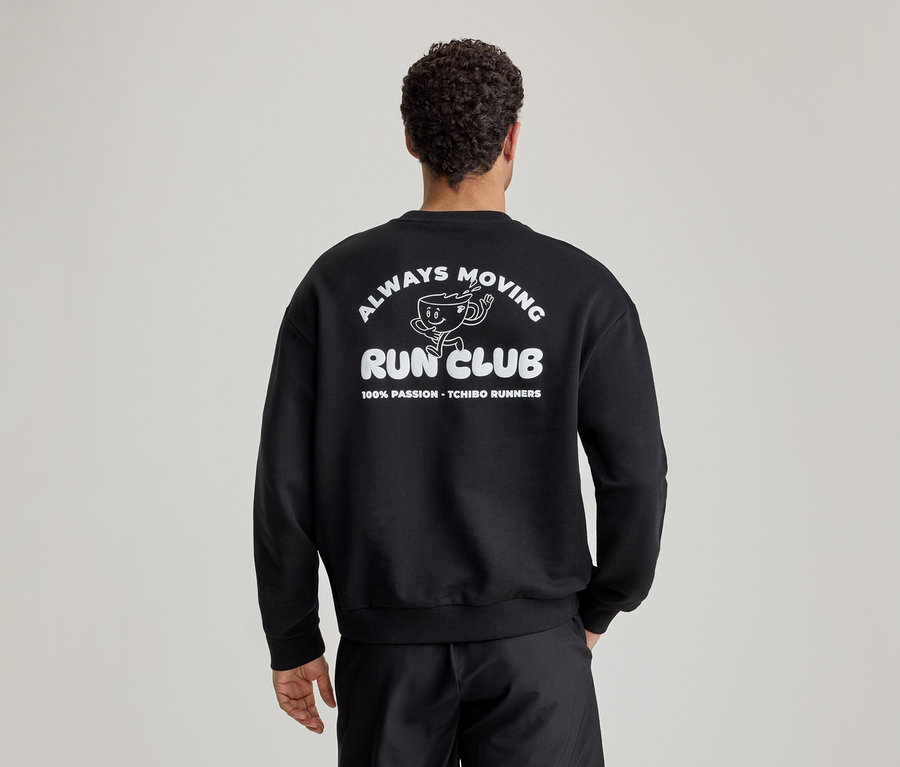 Férfi hátulról, fekete szabadidőfelsőben, melynek hátán fehér 'ALWAYS MOVING RUN CLUB' felirat és futó kávéscsésze rajz látható.