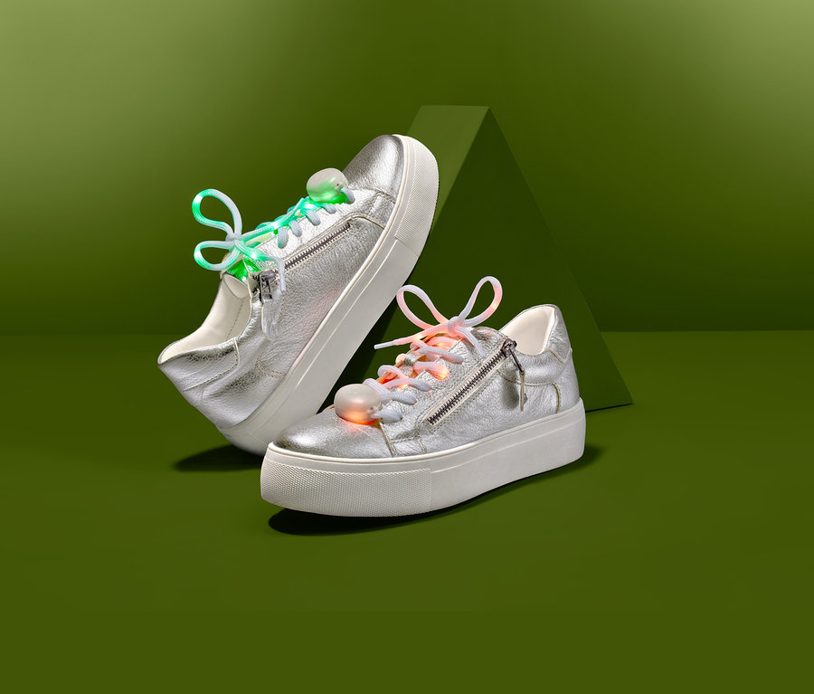 Két ezüst színű tornacipő LED-es cipőfűzővel zöld háttér előtt.