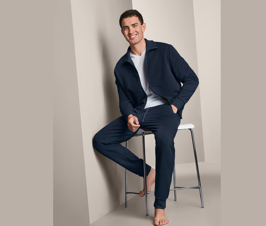 Férfi ül egy széken, sötétkék férfi szabadidő szett van rajta.