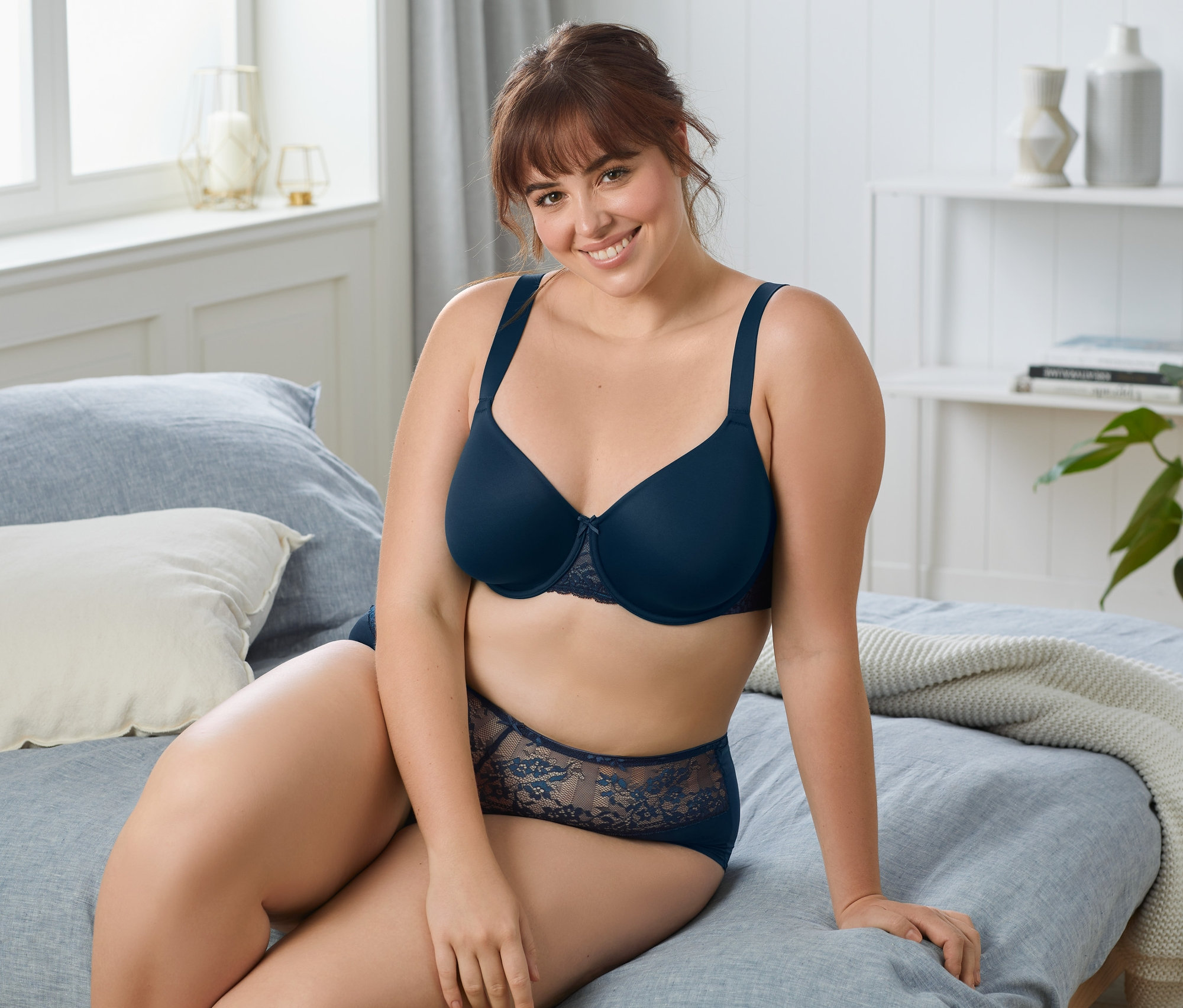 Nő ül az ágyon, sötétkék, merevítős melltartót visel.