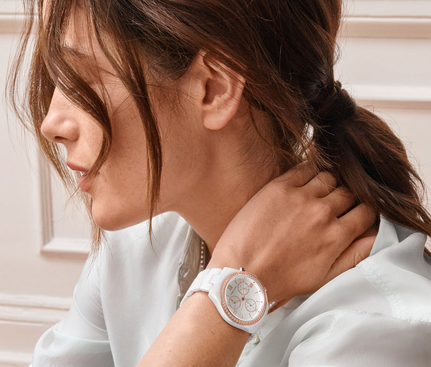 Egy nő megérinti a nyakát, és a csuklóján egy női kerámia kronográfot visel, cirkóniával, fehér.