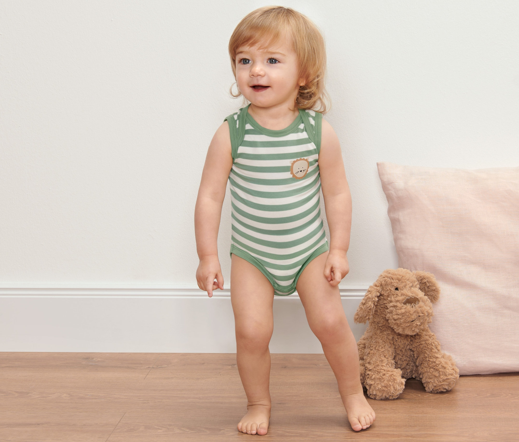 Kisgyermek áll a padlón, és 2 állítható hosszúságú body csecsemőknek van rajta.