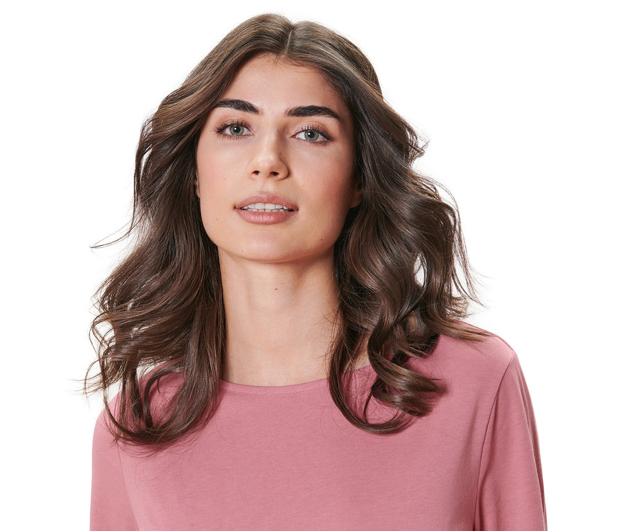 Egy portré egy hullámos barna hajú nőről, aki rózsaszín felsőt visel. A haj hőmentes hajcsavaró készlettel van felcsavarva.