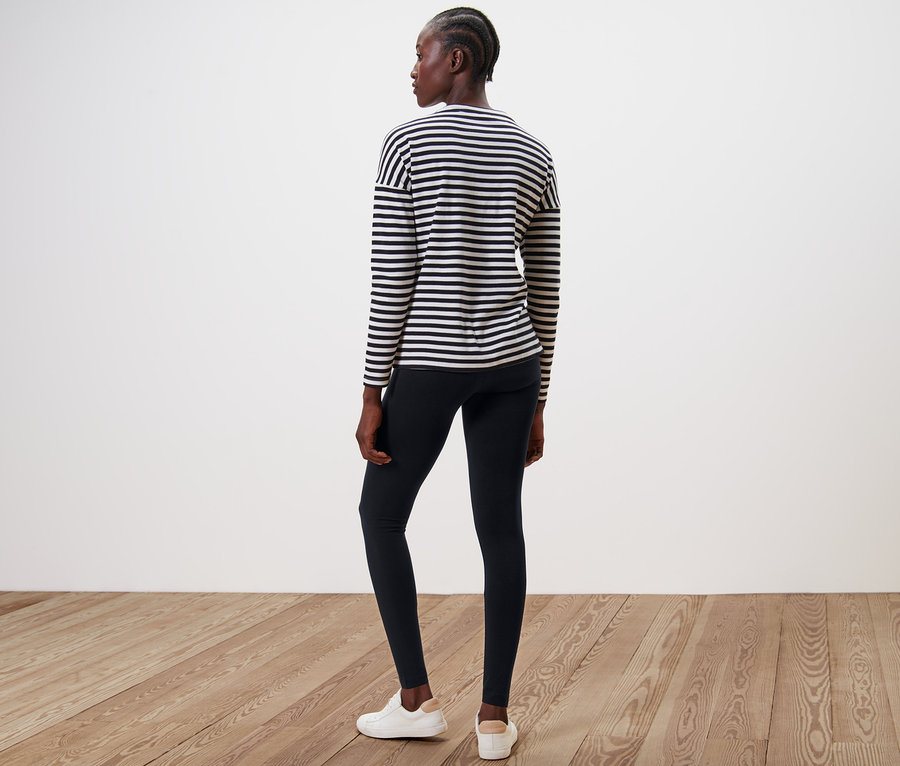 Nő áll háttal a kamerának, fekete leggingset és csíkos felsőt visel.