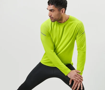 Férfi nyújtja a lábát, neonlime hosszú ujjú funkcionális felsőt és fekete leggingset visel.