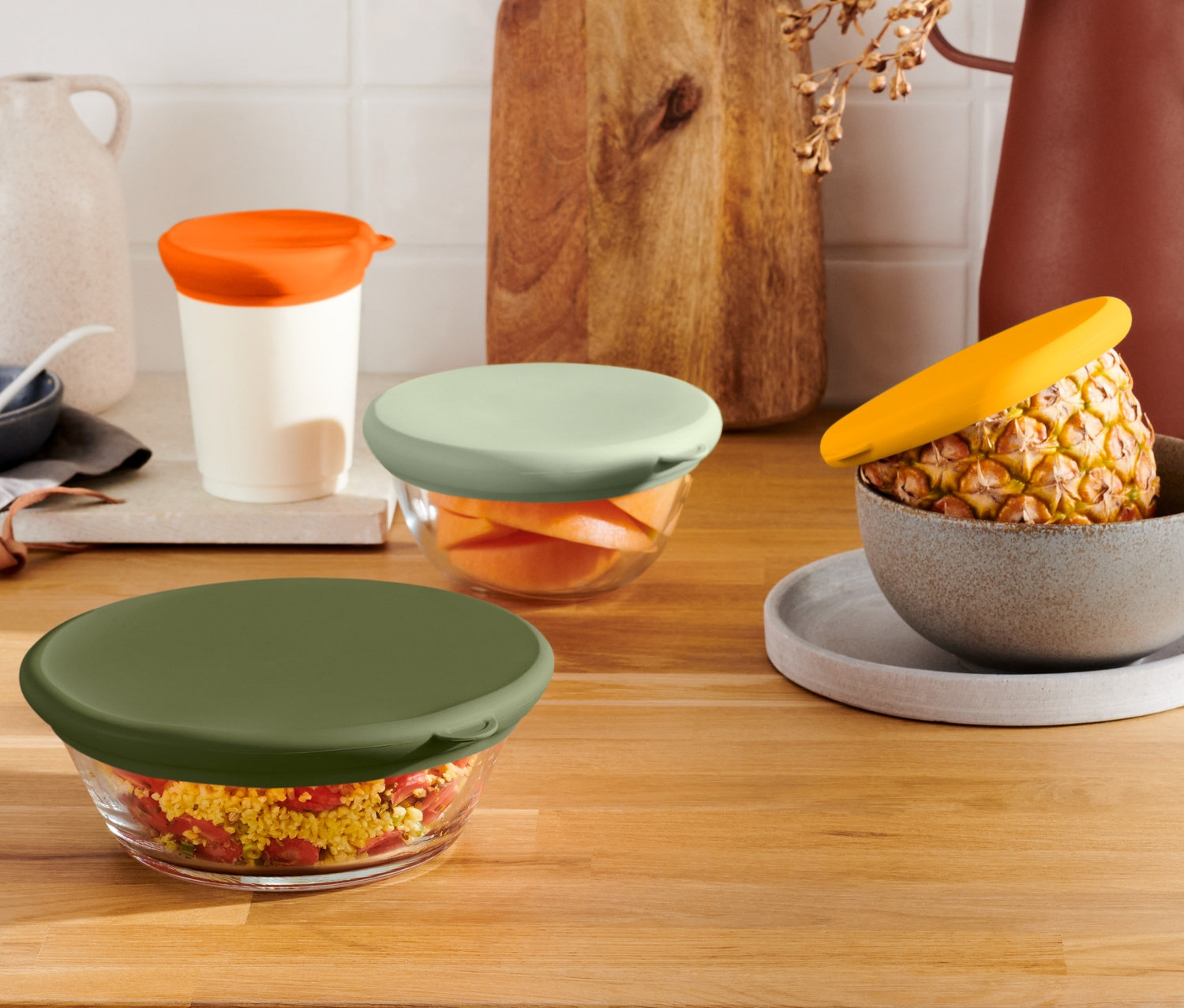 Négy üvegtál különböző színű 4 szilikon frissentartó fedéllel egy fa felületen.