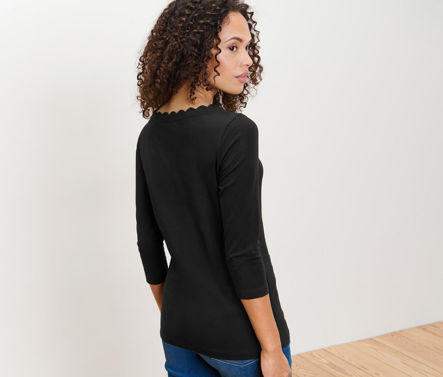 Barna, göndör hajú nő néz a válla fölött, fekete, 3/4-es ujjú felsőt visel.