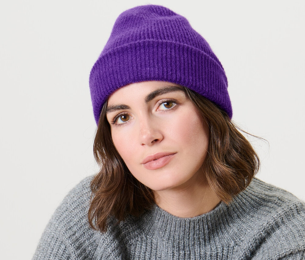 Egy nő ül, lila kötött sapkát visel.