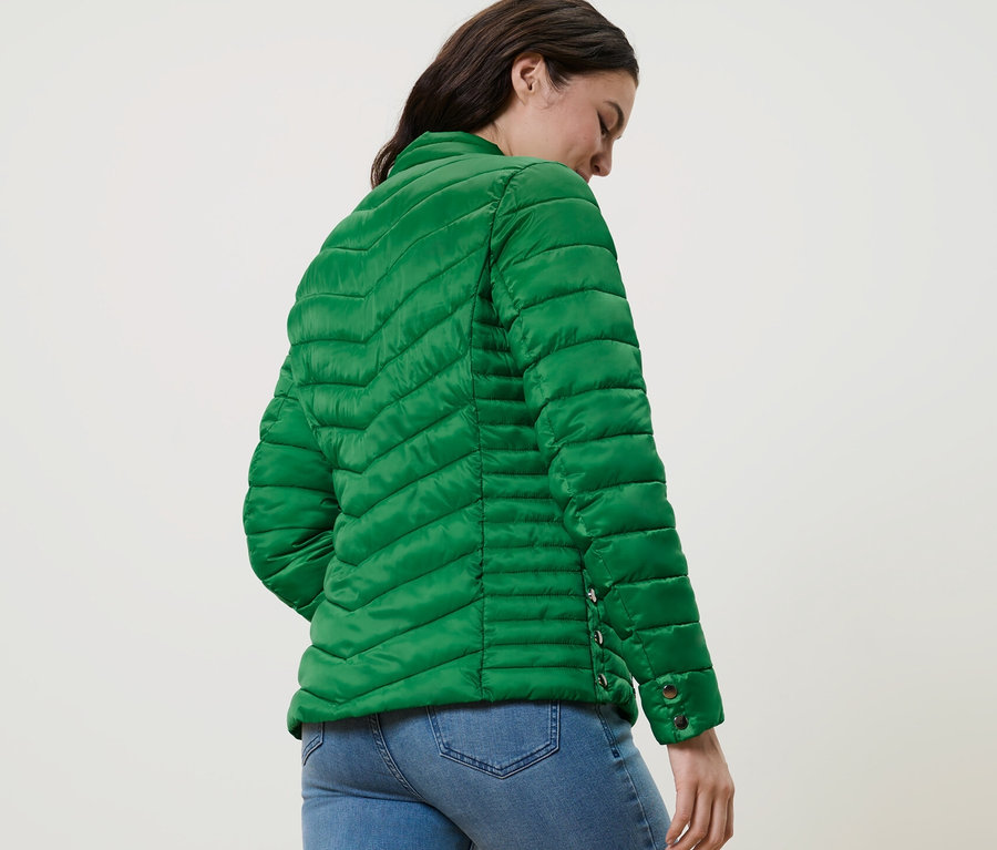 Nő visel zöld steppelt dzsekit és farmert.
