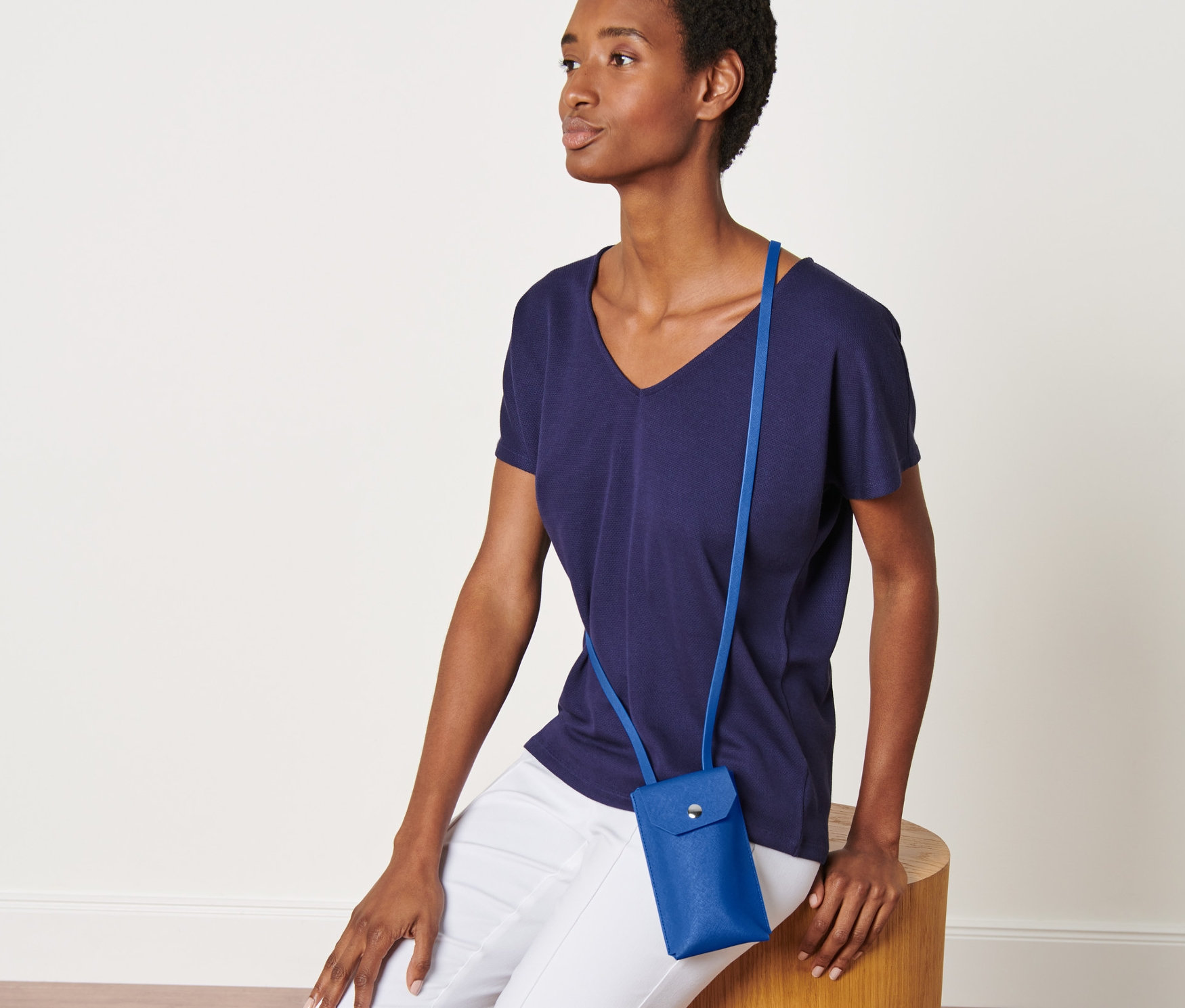 Nő ül egy fa zsámolyon, és egy kék mini oldaltáska van rajta.