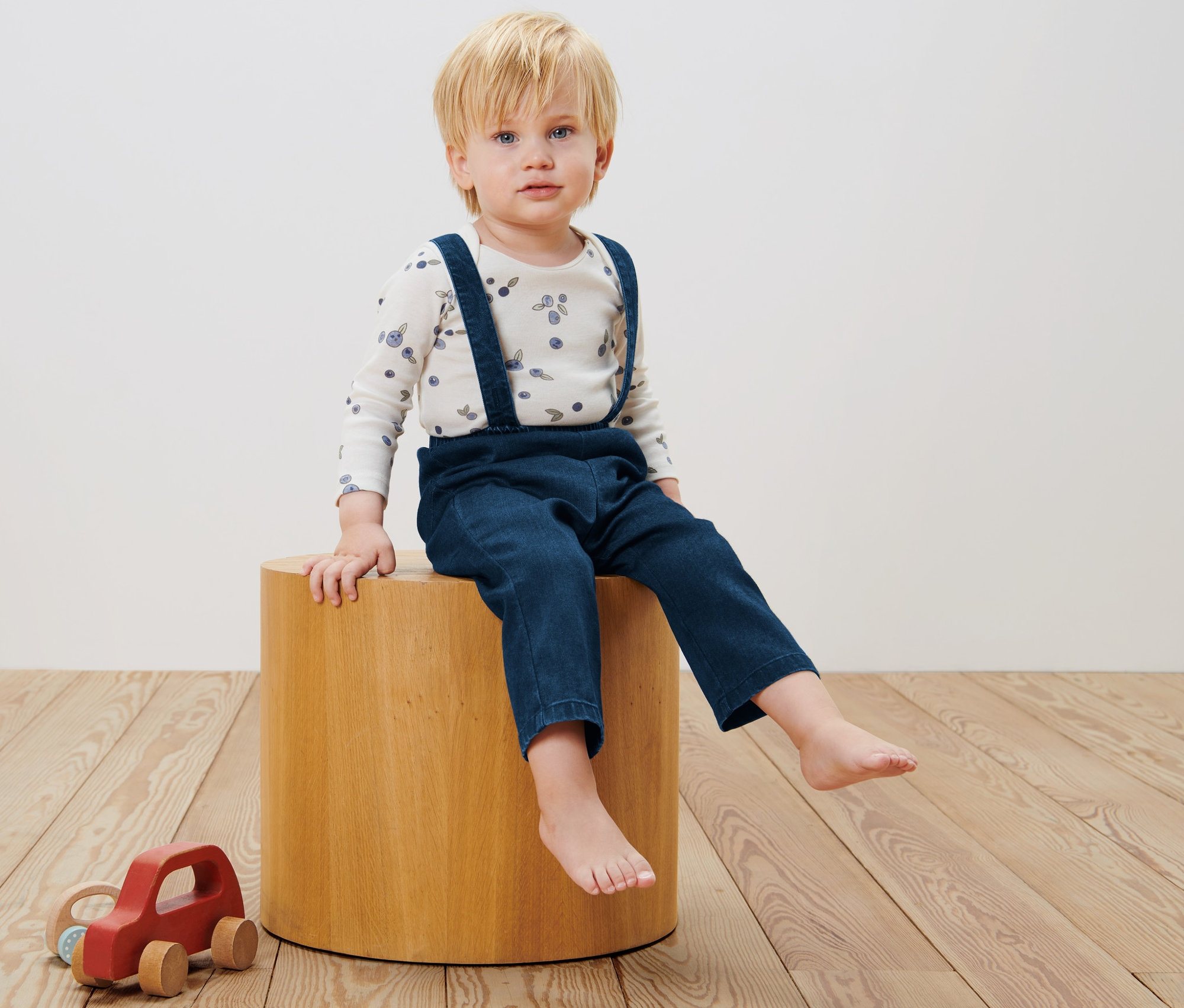 Egy kisfiú ül egy fa ülőkén és kisgyerek sávoly nadrágot visel.