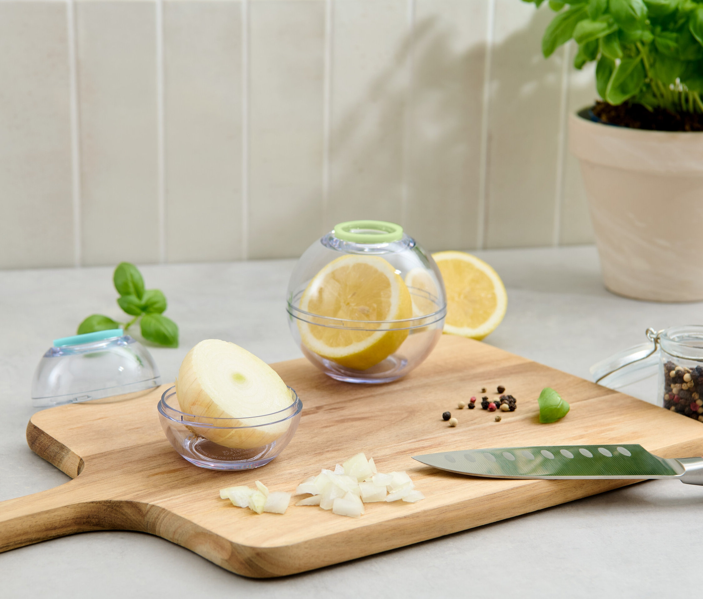 Két frissentartó gömb, egyikben citrom, másikban hagyma, egy vágódeszkán.