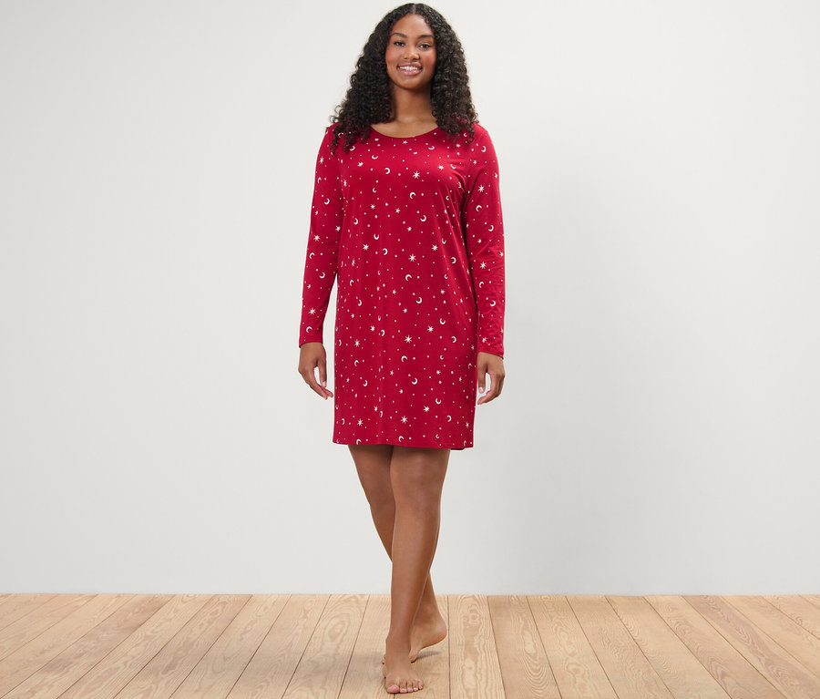 Egy nő áll és mosolyog a kamerába, piros hálóinget visel.