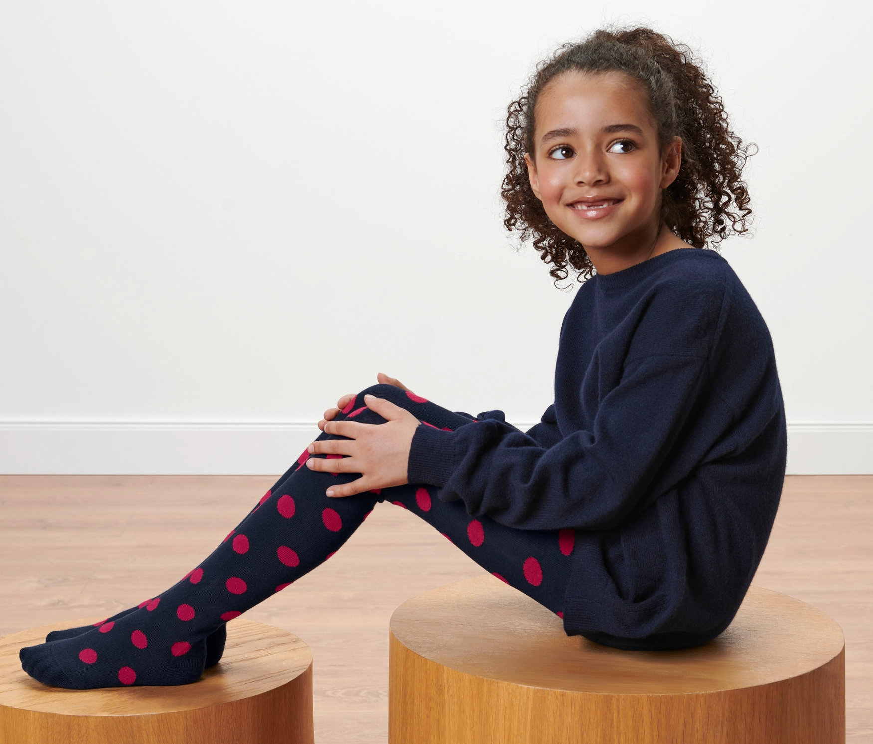 Egy lány ül egy fa zsámolyon, és sötétkék, piros pöttyös harisnyanadrágot visel, 2 kisgyerek harisnyanadrág.